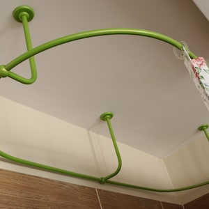 May include: A green metal shower curtain rod is mounted to the ceiling. The rod is curved and has a floral patterned shower curtain hanging from it.