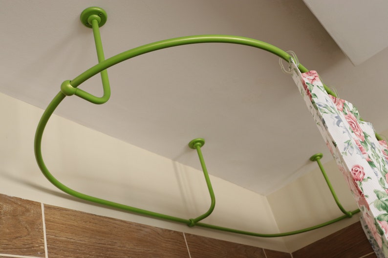 May include: A green metal shower curtain rod is mounted to the ceiling. The rod is curved and has a floral patterned shower curtain hanging from it.