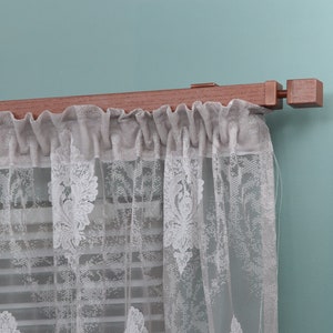 May include: A wooden curtain rod with a white lace curtain hanging from it. The rod is mounted to a light blue wall.