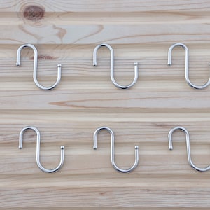 May include: Six silver S-shaped hooks on a wooden surface.