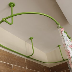 May include: A green metal shower curtain rod with a curved design, mounted to the ceiling. The rod is holding a white and floral patterned shower curtain.