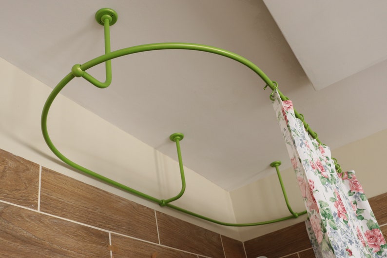 May include: A green metal shower curtain rod with a curved design, mounted to the ceiling. The rod is holding a white and floral patterned shower curtain.