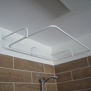 Puede incluir: Barra de cortina de ducha de metal blanco con dos niveles, montada en el techo en un ba&ntilde;o con paredes de azulejos marrones.