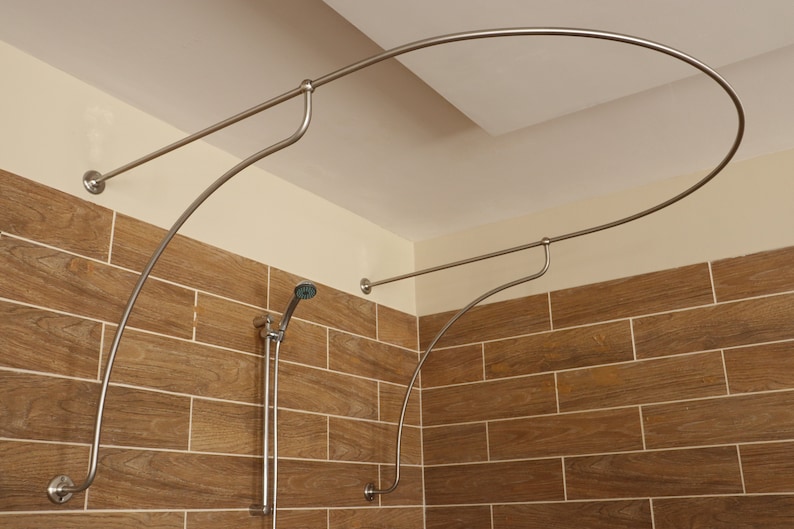 May include: A silver shower curtain rod with a curved design, installed in a bathroom with brown tile walls.