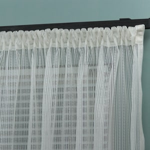 May include: White sheer curtains with a black curtain rod. The curtains have a subtle striped pattern.