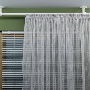Könnte beinhalten: Weiße, an der Decke montierte Gardinenstange mit weißen, durchsichtigen Gardinen, die daran hängen. Die Gardinen befinden sich vor einem Fenster mit weißen Jalousien.