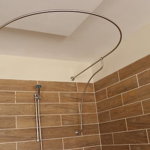 May include: A silver shower curtain rod with a curved design, installed in a bathroom with brown tile walls.