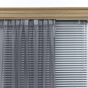 May include: A window with a wooden trim and a set of white blinds. The blinds are partially open, revealing a sheer gray curtain behind them.