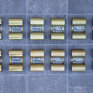 Könnte beinhalten: Eine Musterkarte mit 12 verschiedenen Messing-Oberflächen, die mit ihren Namen und Nummern beschriftet sind. Die Oberflächen umfassen Glanz, Matt, Gebürstet, Hell Alt, Mittel Alt und Dunkel Alt.