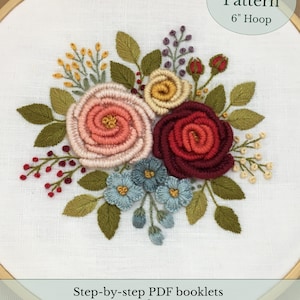 以下が含まれることがあります： 15cmのフープに刺繍された花の模様。ピンクと赤の色合いのバラの花束が特徴で、青と黄色のアクセントがあります。「PDF Pattern」と「6" Hoop」の文字が見えます。
