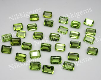 May include: A collection of 25 green peridot gemstones, cut in an emerald shape. The stones are faceted and have a translucent appearance.