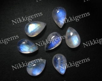 May include: Seven pearlescent white teardrop-shaped moonstone cabochons with a blue iridescent sheen on a black background.  The stones are arranged in a semi-circle with the text "Nikkigems" appearing multiple times around the stones.