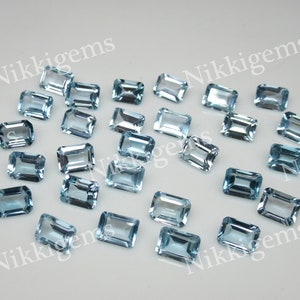 May include: A collection of 20 light blue topaz gemstones, cut in an emerald shape. The gemstones are faceted and have a translucent appearance.