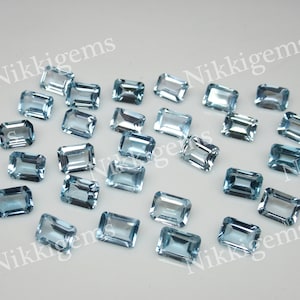 May include: A collection of 20 light blue topaz gemstones, cut in an emerald shape. The gemstones are faceted and have a translucent appearance.