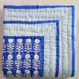 May include: A blue and white quilt with a floral pattern and chevron design. The quilt features a vibrant blue floral section and a light blue and white chevron pattern. The edges are trimmed with a solid blue border.