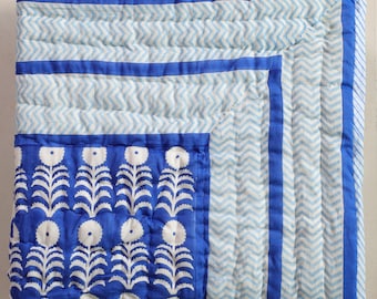 May include: A blue and white quilt with a floral pattern and chevron design. The quilt features a vibrant blue floral section and a light blue and white chevron pattern. The edges are trimmed with a solid blue border.