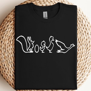 Pode incluir: Camiseta preta com um gráfico branco de um esquilo, dois patos e um ovo. O gráfico é uma ilustração estilizada da palavra "WOO"