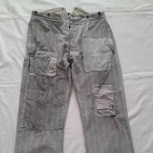 May include: Light gray striped pants with multiple fabric patches. The patches are in various colors and patterns, including a checkered design. The pants have a button closure and appear to be vintage or repurposed.