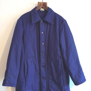 May include: A solid royal blue jacket featuring a pointed collar, a front button closure with five visible dark buttons, and two slanted front pockets. The jacket has long sleeves and a straight hemline, providing a simple and functional design.