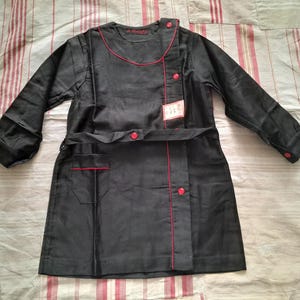 May include: A black uniform with red trim and buttons. The uniform has long sleeves, a belt, and a pocket. The collar and seams are accented with red piping. A tag is attached to the front.