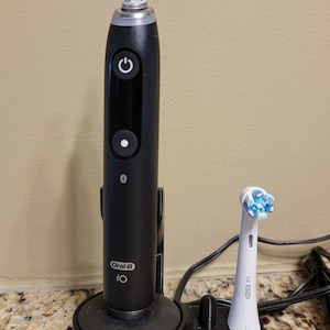 May include: A black electric toothbrush with a white charging base and a white electric toothbrush head with blue bristles. The toothbrush is plugged into an outlet.