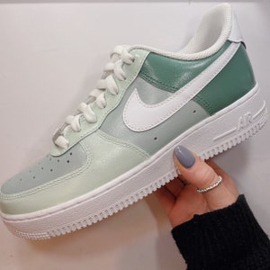 Op de afbeelding: Een op maat gemaakte Air Force 1 sneaker in groen- en wittinten. De schoen heeft een witte zool, veters en Nike swoosh. De bovenkant is een verloop van licht- naar donkergroen. Het woord "AIR" is zichtbaar op de zijkant van de zool.