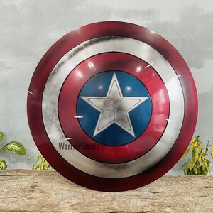 May include: A round shield with a red, white, and blue color scheme. The shield features a large white star on a blue circle in the center, surrounded by concentric rings of silver, white, and red. The text "WarriorShield" is visible.