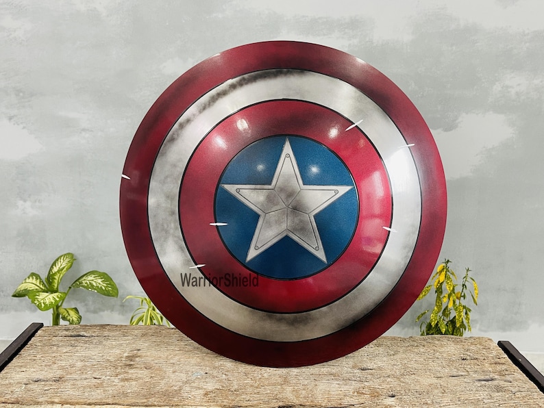 May include: A round shield with a red, white, and blue color scheme. The shield features a large white star on a blue circle in the center, surrounded by concentric rings of silver, white, and red. The text "WarriorShield" is visible.