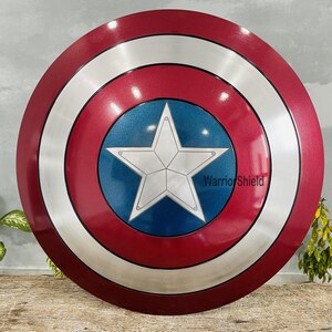 May include: A round shield with a red, white, and blue color scheme. The shield features a large white star on a blue center, surrounded by a silver ring and a red outer edge. The text "Warrior Shield" is visible on the shield.
