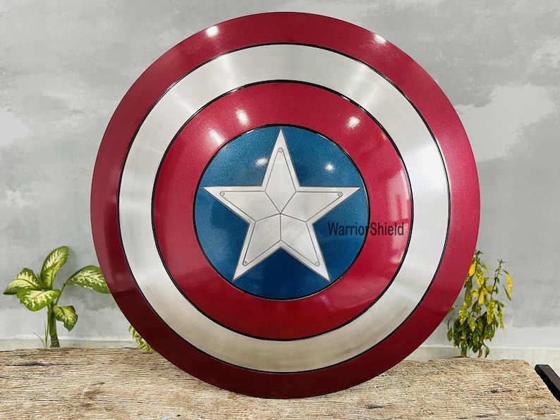 May include: A round shield with a red, white, and blue color scheme. The shield features a large white star on a blue center, surrounded by a silver ring and a red outer edge. The text "Warrior Shield" is visible on the shield.