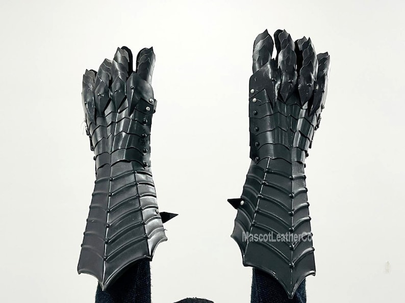 May include: A pair of black leather gauntlets with claw-like fingers. The gauntlets are made of segmented plates and have a textured surface. The gauntlets are raised in the air, with the fingers pointing upwards.
