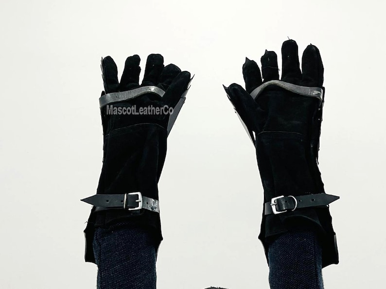 May include: A pair of black leather gloves with metal finger guards and wrist straps. The gloves are worn by a person with their arms raised.