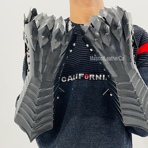 May include: A pair of black leather gauntlets with a spiky, dragon-scale design. The gauntlets are worn by a person wearing a black sweater with the word "CALIFORNIA" printed on it. The text "MascottLeatherCo" is also visible on the sweater.