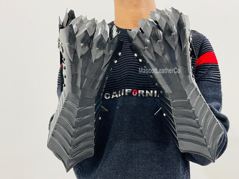 May include: A pair of black leather gauntlets with a spiky, dragon-scale design. The gauntlets are worn by a person wearing a black sweater with the word "CALIFORNIA" printed on it. The text "MascottLeatherCo" is also visible on the sweater.
