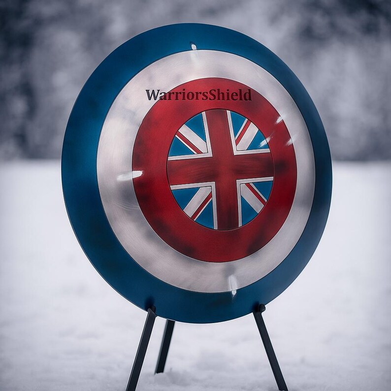 May include: A round shield with a blue outer ring, a silver center, and a red and white Union Jack design in the middle. The text "WarriorsShield" is printed on the shield. The shield is propped up on a black stand.