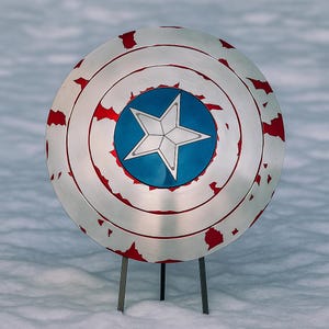 Puede incluir: Un escudo plateado con una estrella azul y blanca en el centro, rodeado de c&iacute;rculos conc&eacute;ntricos y detalles rojos. El escudo est&aacute; apoyado en un soporte met&aacute;lico, sobre un fondo nevado.