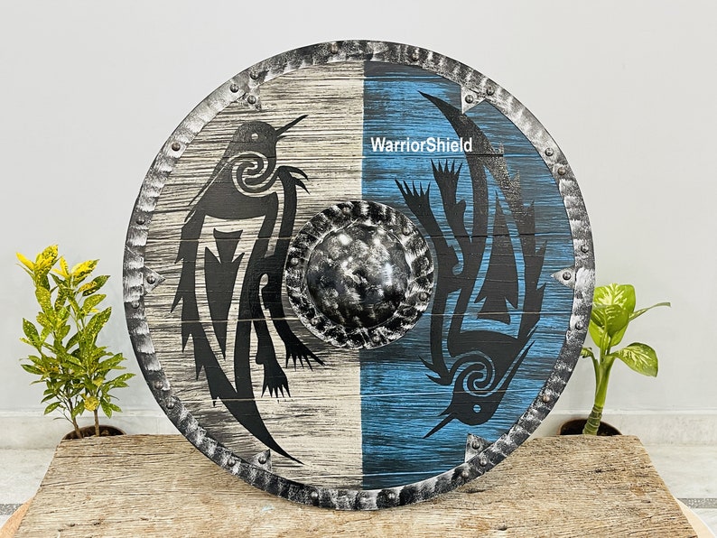 May include: A round wooden shield with a black and white design on one side and a blue and black design on the other side. The shield has a metal rim with rivets and a metal boss in the center. The text "WarriorShield" is printed on the shield.