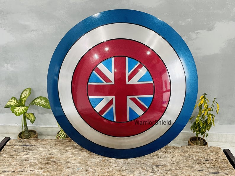 May include: A blue, white, and red Captain America shield with a Union Jack design in the center. The shield is made of metal and has a shiny finish. The text "WarriorShield" is printed on the shield.