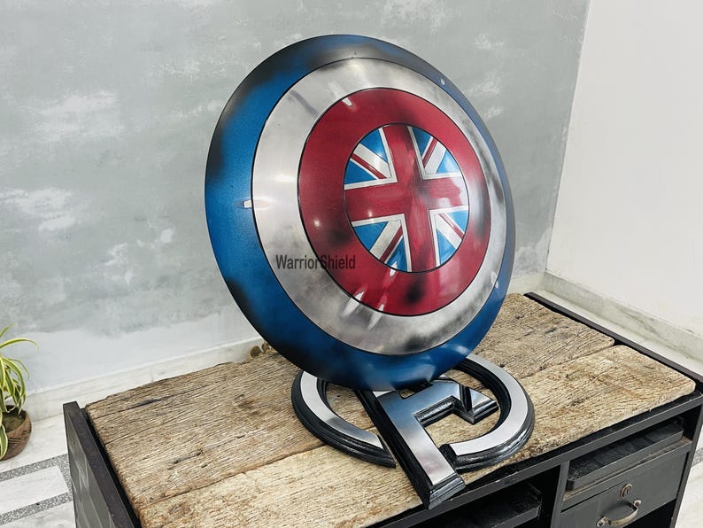 May include: A blue, red, and white Captain America shield with a Union Jack design in the center. The shield is on a stand with the letter "A" on it. The text "Warrior Shield" is visible on the shield.