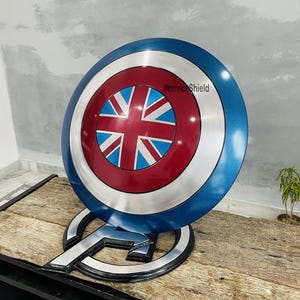 May include: A blue and red Captain America shield with a Union Jack design in the center. The shield is on a wooden stand with the text "Warrior Shield" on the shield.