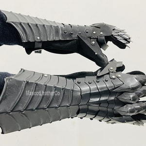 May include: A pair of black leather gauntlets with metal plates and spikes. The gauntlets have a claw-like design on the fingers. The text "MascotLeatherCo" is visible on the lower gauntlet.
