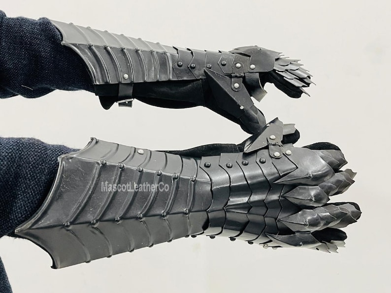 May include: A pair of black leather gauntlets with metal plates and spikes. The gauntlets have a claw-like design on the fingers. The text "MascotLeatherCo" is visible on the lower gauntlet.