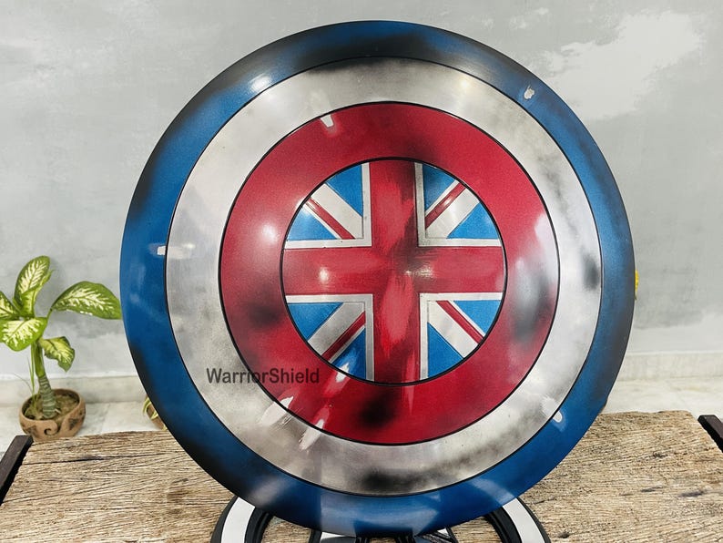 May include: A round, blue and silver Captain America shield with a red, white, and blue Union Jack design in the center. The shield has a distressed, weathered look. The text "WarriorShield" is printed on the shield.