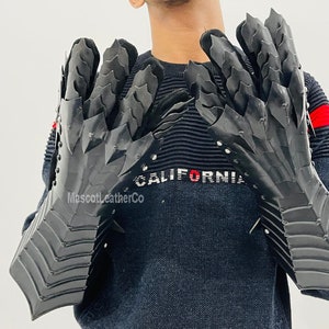 May include: A pair of black leather gauntlets with a dragon scale design. The gauntlets have a pointed tip and are worn by a person with the word "CALIFORNIA" on their sweater.