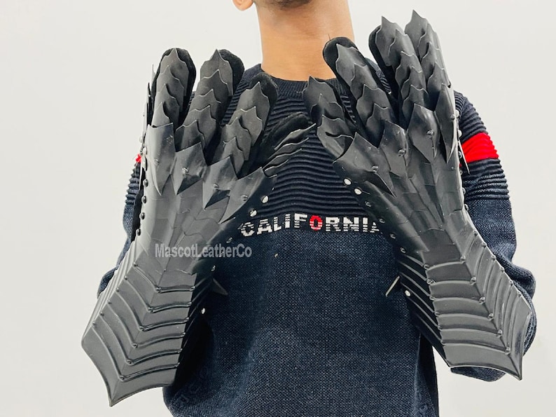 May include: A pair of black leather gauntlets with a dragon scale design. The gauntlets have a pointed tip and are worn by a person with the word "CALIFORNIA" on their sweater.