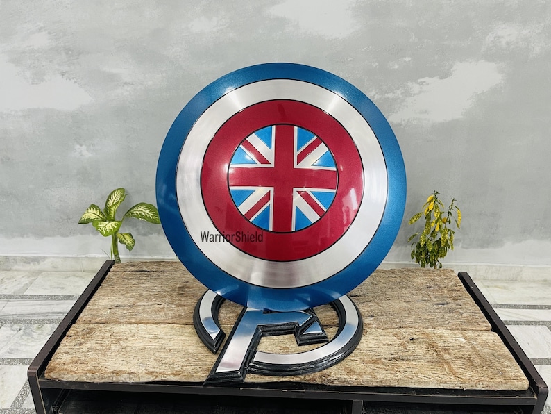 May include: A blue, red, and white Captain America shield with a Union Jack design in the center. The shield is on a stand with the Avengers logo.