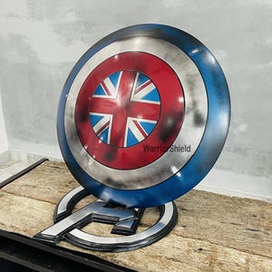 May include: A red, white, and blue Captain America shield with a Union Jack design in the center. The shield is on a stand with the text "Warrior Shield" on it.