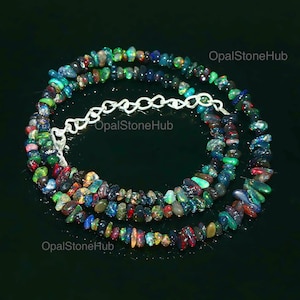Puede incluir: Un collar de múltiples hilos hecho de pequeñas cuentas de ópalo irregulares e iridiscentes en tonos de azul, verde, rojo y negro. El collar está enhebrado en una cadena de plata con un cierre.