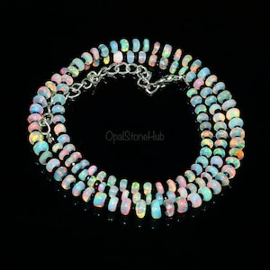 May include: A multi-strand necklace made of iridescent white opal beads with a silver clasp. The necklace is on a black background.
