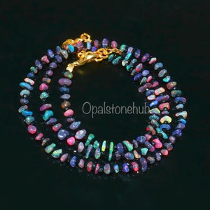 May include: A multi-strand necklace composed of colorful, irregularly shaped opal beads. The beads display a variety of colors, including pink, blue, green, and purple. The necklace is secured with a gold-colored clasp.